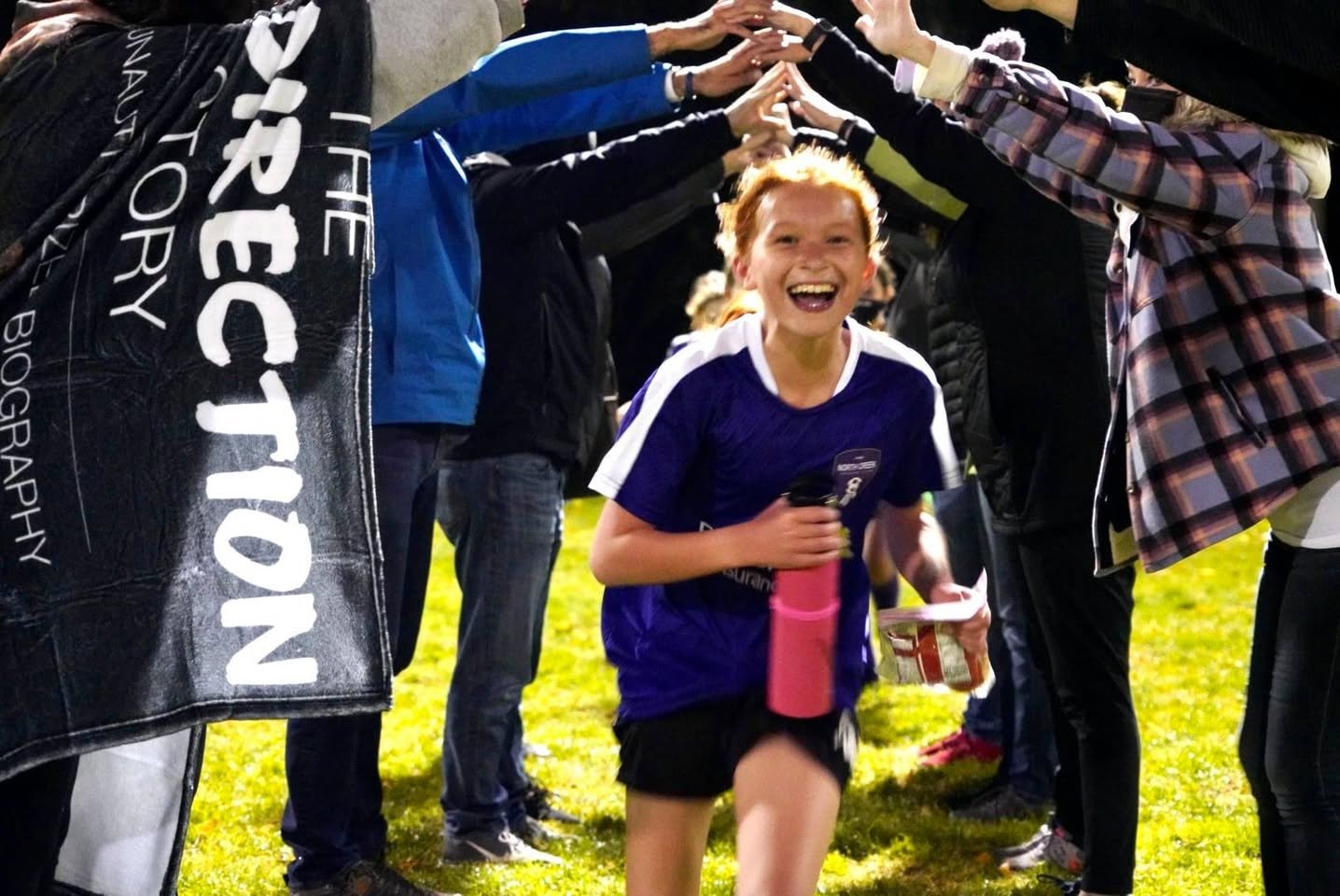 A smiling runner finishes a race while spectators form a tunnel of hands overhead.