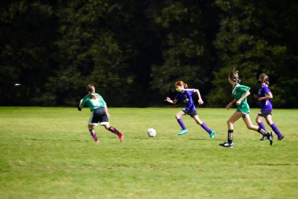 Young soccer players in green and purple kits compete for the ball on a sunlit grass field. The lower frames capture details of movement and ball positioning.
