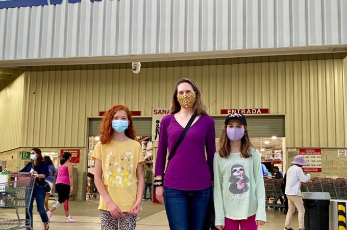 A family poses outside the Costco warehouse, with the prominent red and blue logo visible above them.