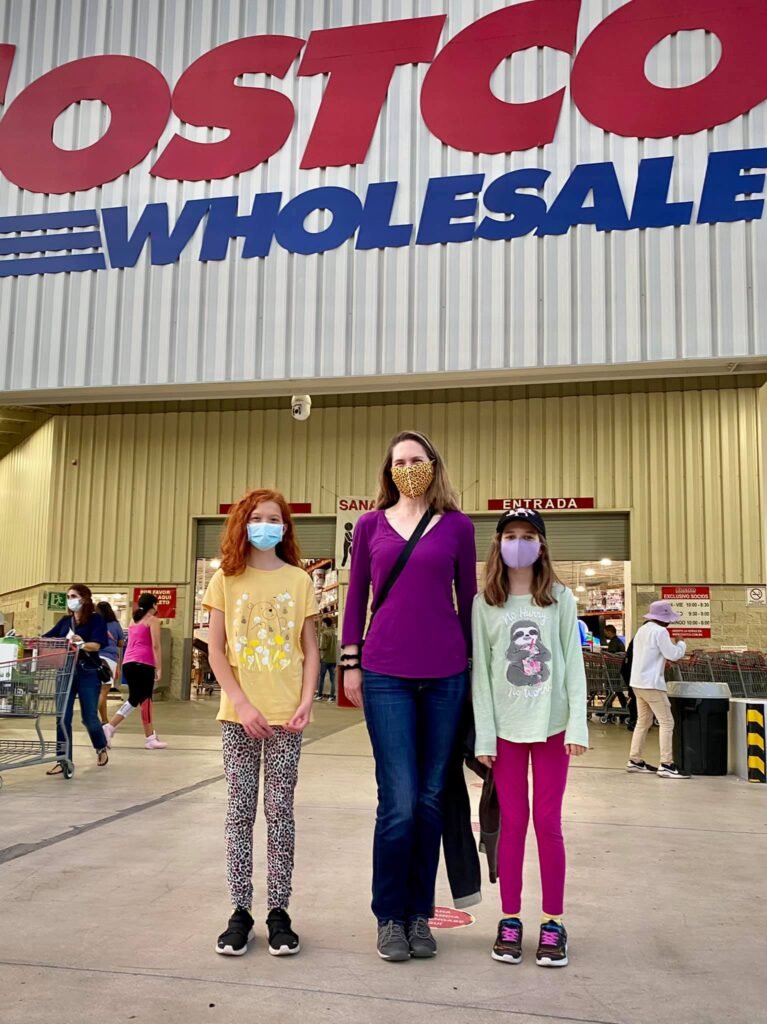 A family poses outside the Costco warehouse, with the prominent red and blue logo visible above them.