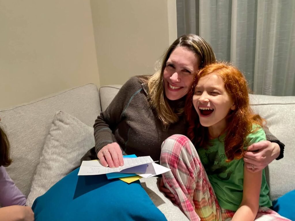Two people laughing together on a couch while reading a paper, capturing a happy family moment.