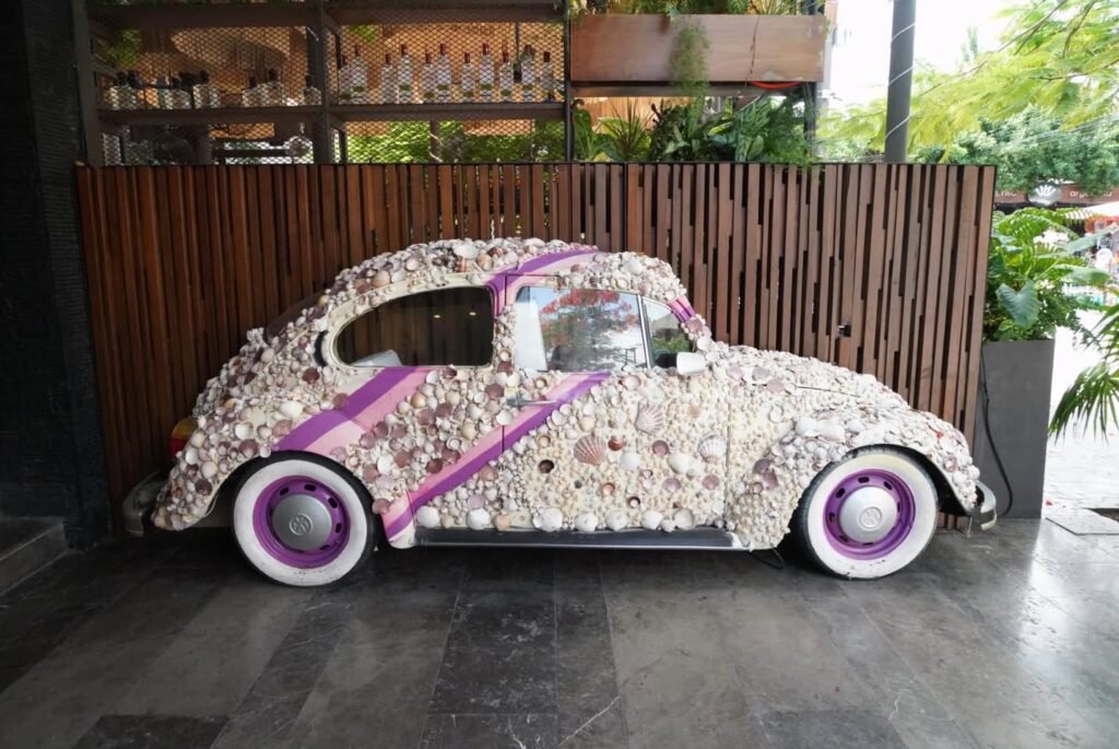 A vintage beetle car sculpture covered entirely in white and purple sneakers and display stand.