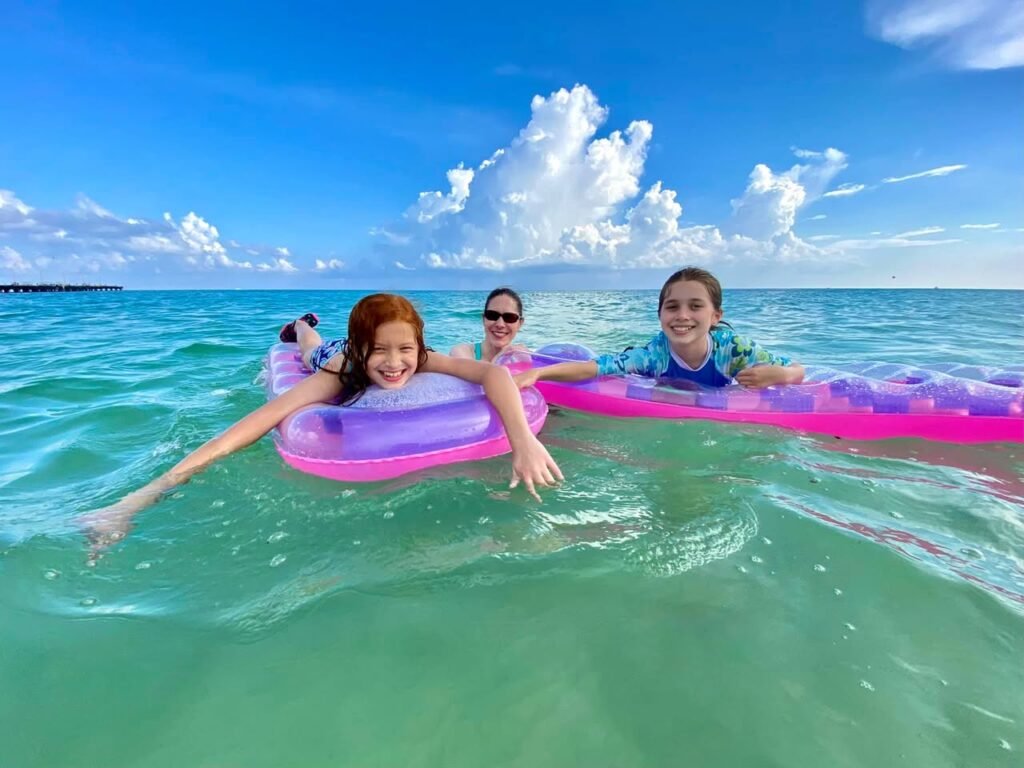 People floating on inflatable rings in turquoise water under a blue sky with white clouds.