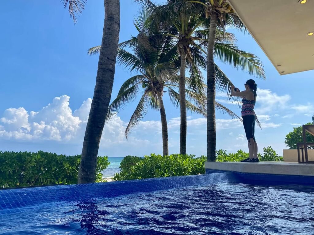 A serene view of an infinity pool overlooking the ocean with tall palm trees swaying in the breeze under a bright blue sky. This picturesque scene highlights the ultimate destination for peaceful tropical relaxation.