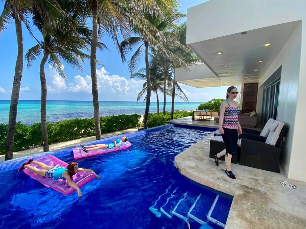 A sunny day at a resort with a pool and palm trees overlooking the ocean.