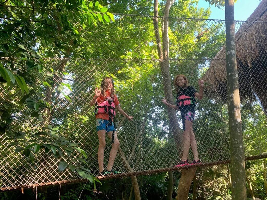 Two people crossing a rope bridge in a jungle resort.
