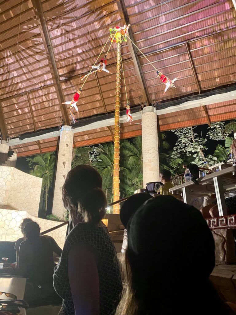 A person is seated and looking towards a traditional bamboo structure with a decorative hanging ornament.