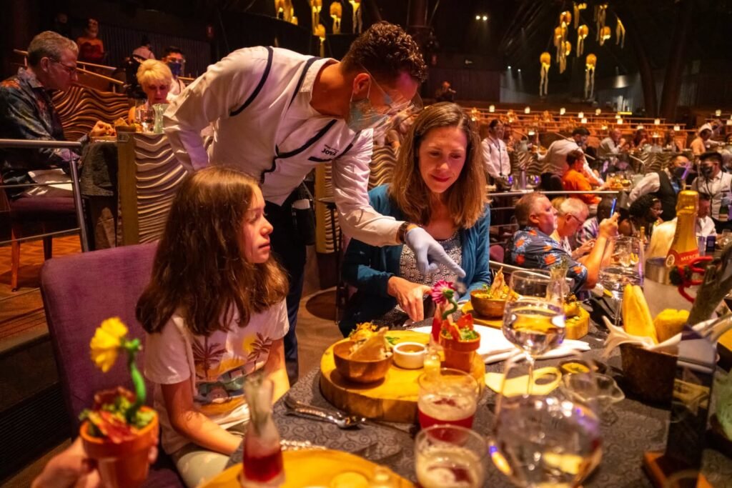 Audience members enjoying a meal at a live dinner show with performers interacting with guests. Multiple views of the atmosphere and tables with food.