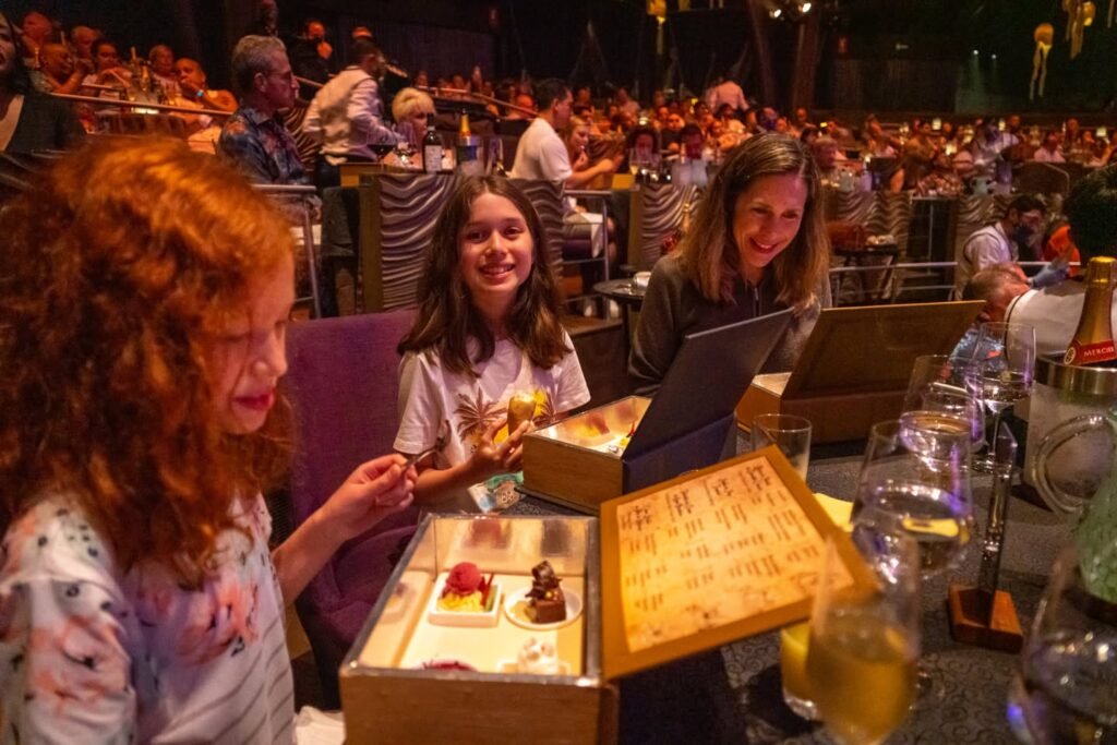 Two girls sit at a table in a concert hall, enjoying desserts and drinks with a view of the audience.
