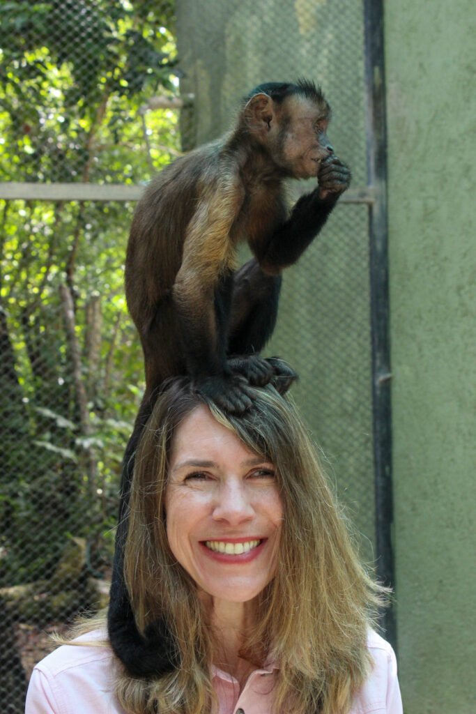 A monkey sits on a woman's head near a zoo enclosure fence.