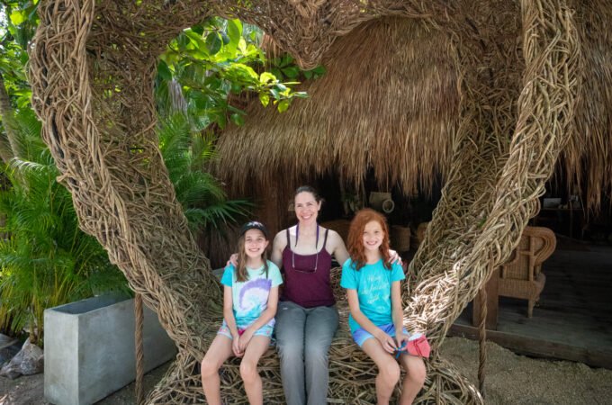 A family poses for a photo inside a large heart-shaped sculpture made of woven natural fibers.
