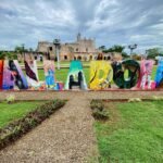 Tulum Large colorful metal sculpture spelling "Mi Amor" in a park, with the historic Mission San José building visible in the background.