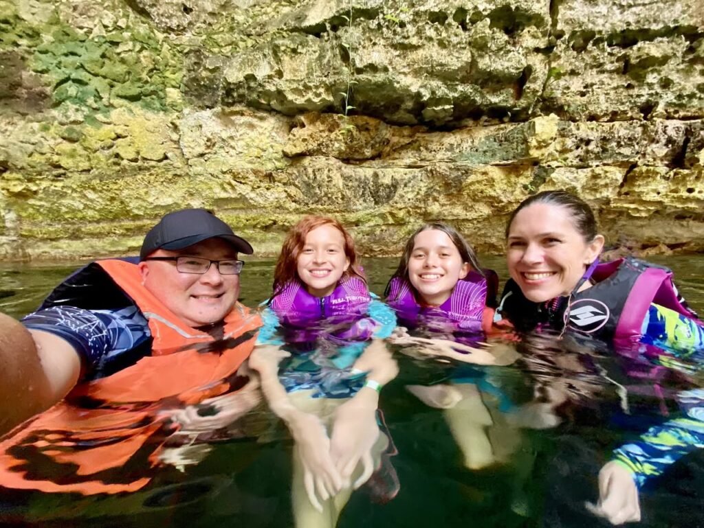 A group of four wearing life jackets enjoy a refreshing dip in a rocky creek, surrounded by natural stone formations.