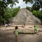 A large stone pyramid rises from the jungle with children playing in the foreground.