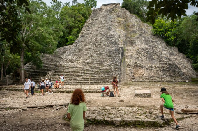 A large stone pyramid rises from the jungle with children playing in the foreground.