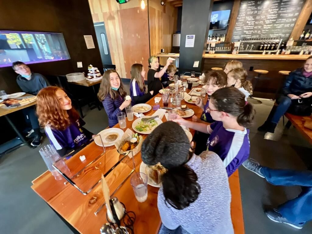 A group of people enjoys a meal at a long wooden table in a restaurant with a modern interior.