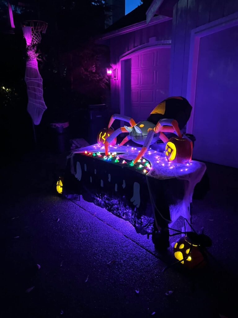A table decorated with Halloween treats and props illuminated by colorful lights in a dark setting.
