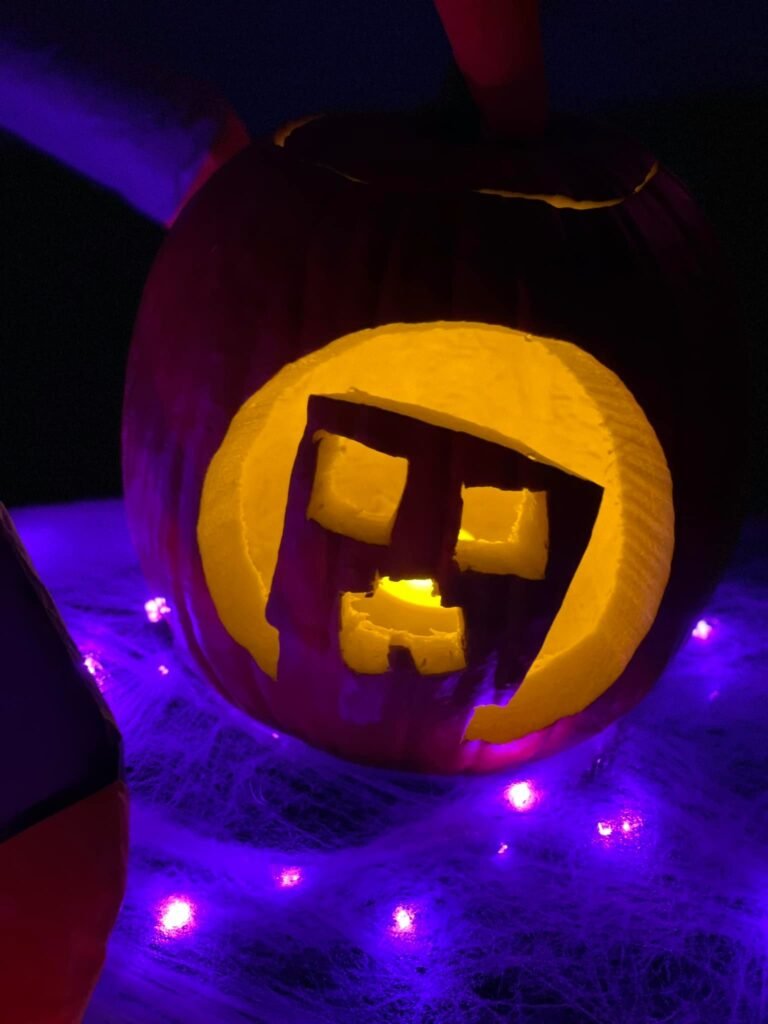 A lit jack-o'-lantern with a Minecraft-style face glowing in purple light.