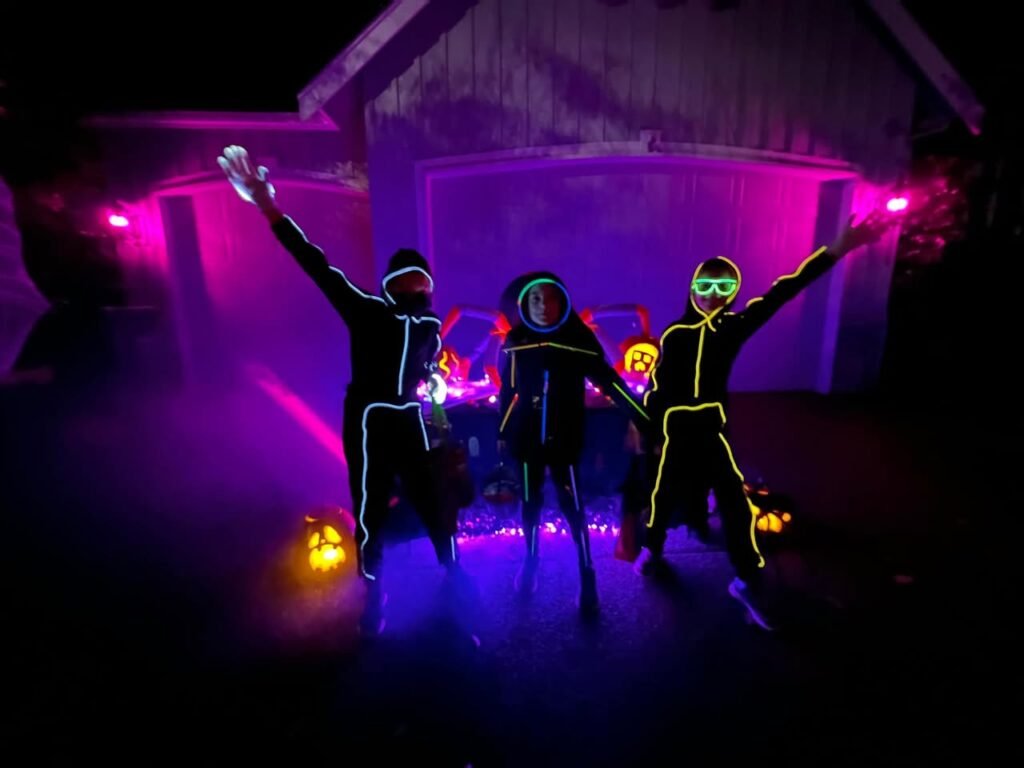 Floating pumpkin-shaped drones with lit interiors glowing in purple light. People with neon face paint dance among floating pumpkin lights.