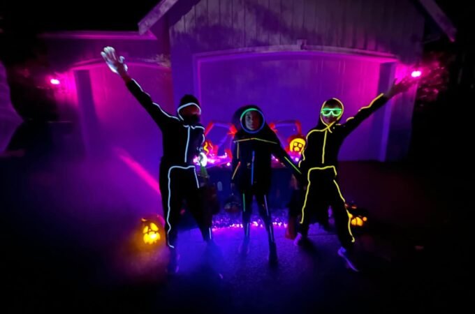 Floating pumpkin-shaped drones with lit interiors glowing in purple light. People with neon face paint dance among floating pumpkin lights.