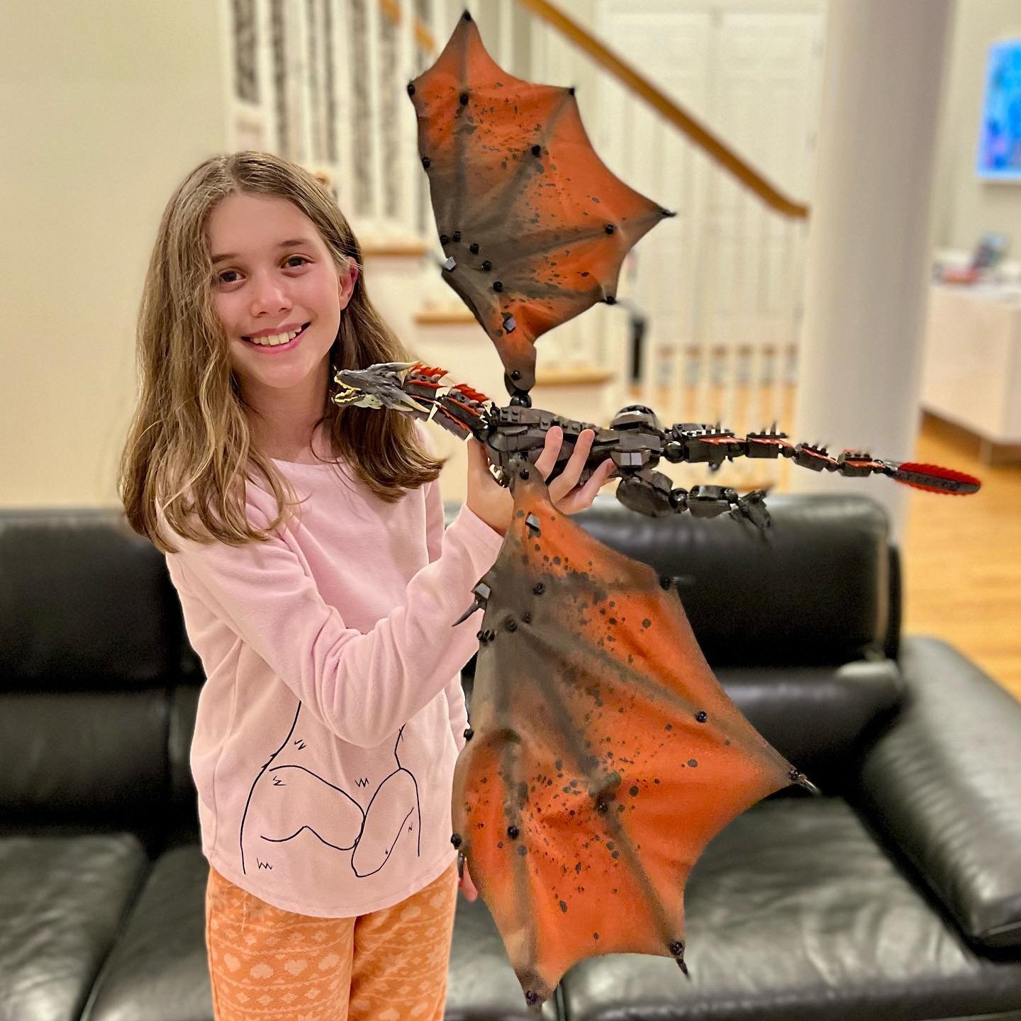 Drogon A girl in a living room smiles while holding a large robotic dragon drone with vibrant orange wings.