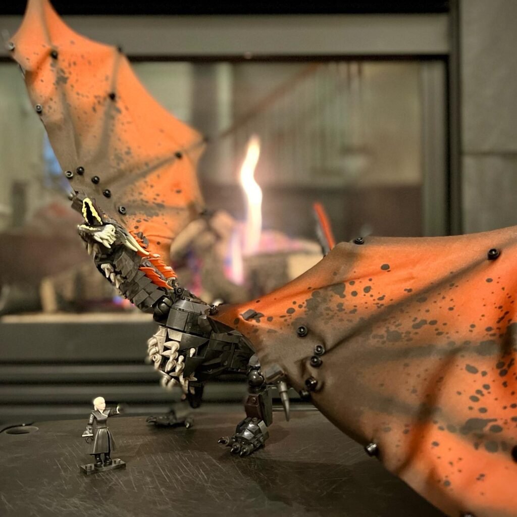 A close-up of a model dragon with bright orange wings on a small figure on a dark surface.