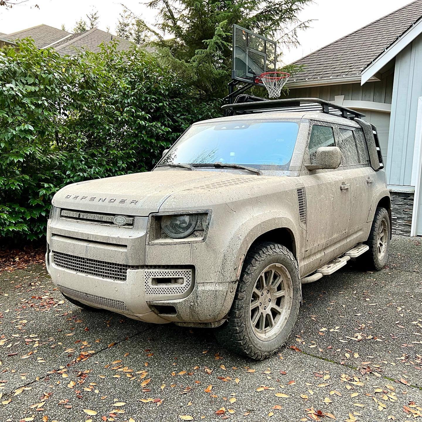 DirtFish A mud-covered Land Rover Defender parked in a driveway. The vehicle shows signs of recent off-road adventure in the Pacific Northwest.