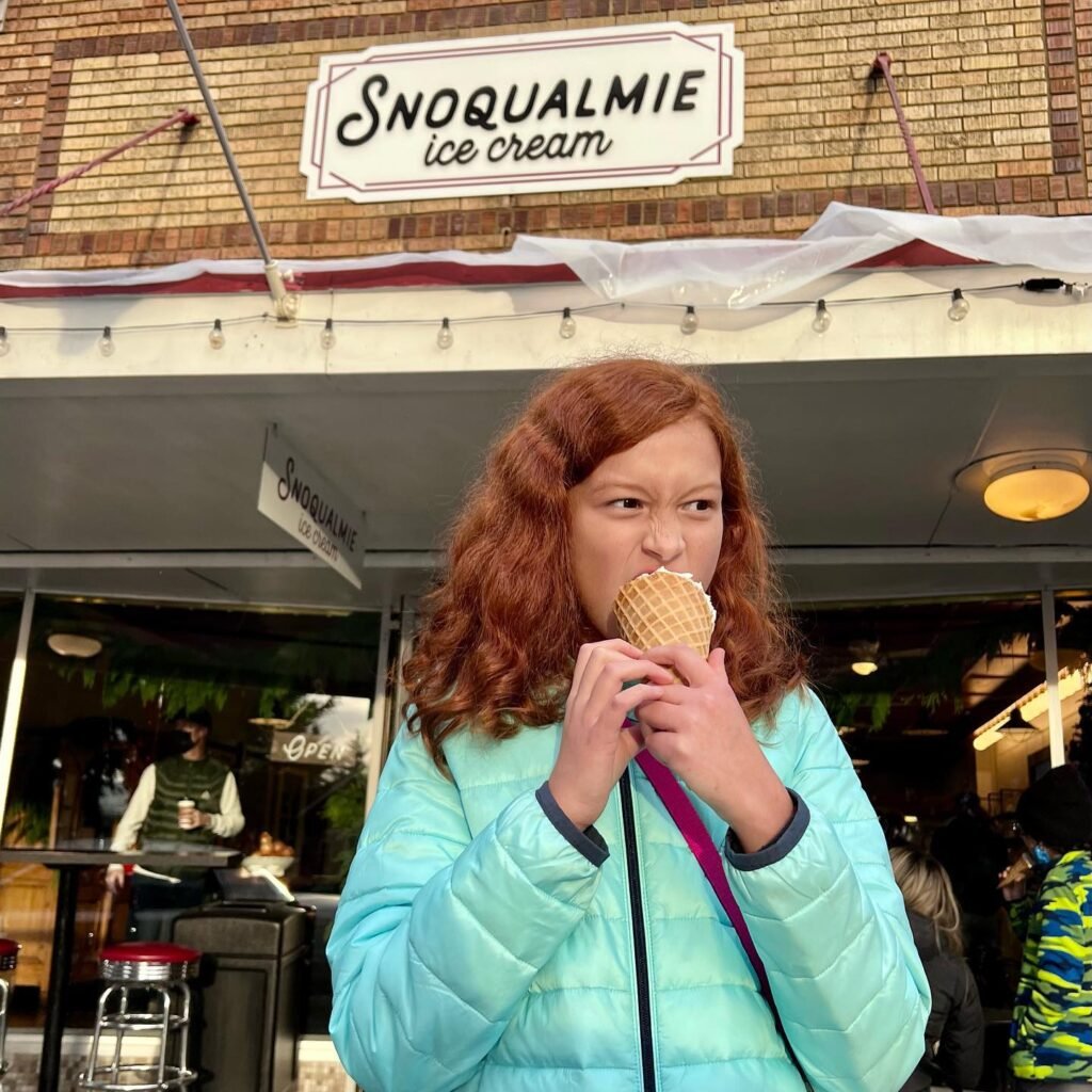 A person enjoying an ice cream cone in front of a Snoqualmie Ice Cream shop. The scene highlights a classic treat in a pleasant outdoor setting.