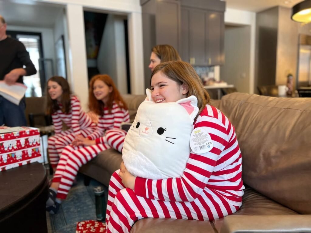 A group of people wearing red and white striped pajamas gathered in a living room, with one person hugging a white cat pillow.