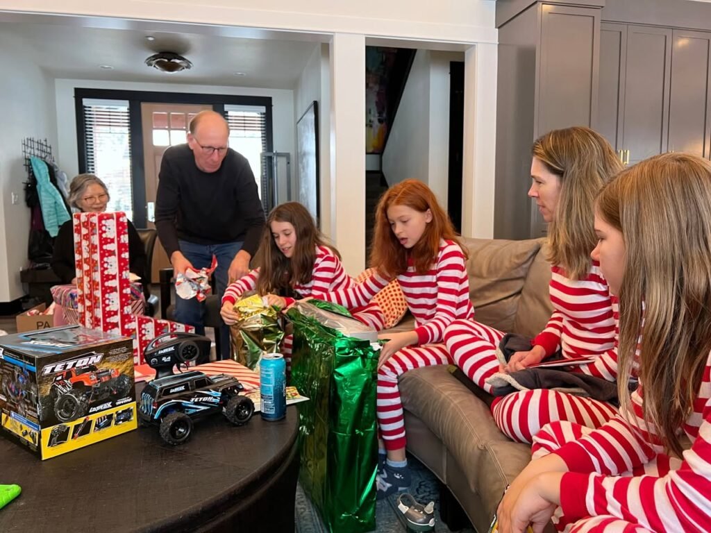 Family gathered in a cozy living room opening gifts together, surrounded by holiday energy and warm moment.