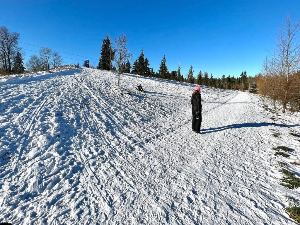A hiker on a trail through a snowy mountain landscape under a clear blue sky.