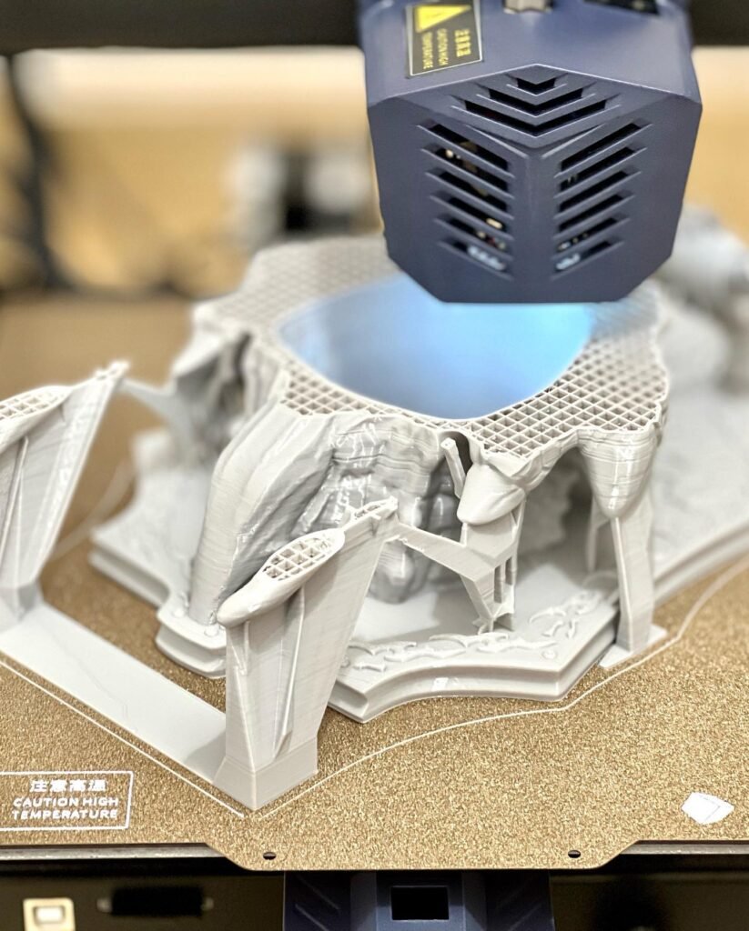 A black 3D printer head with blue light cures a white vat of resin. The machine is building a detailed white object with intricate structures.