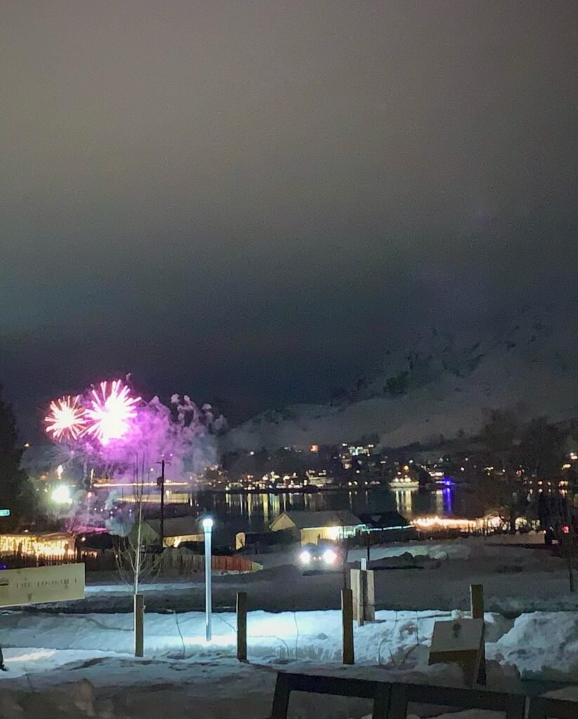 Vibrant fireworks burst in a dark sky above a snowy mountain town during a winter celebration.