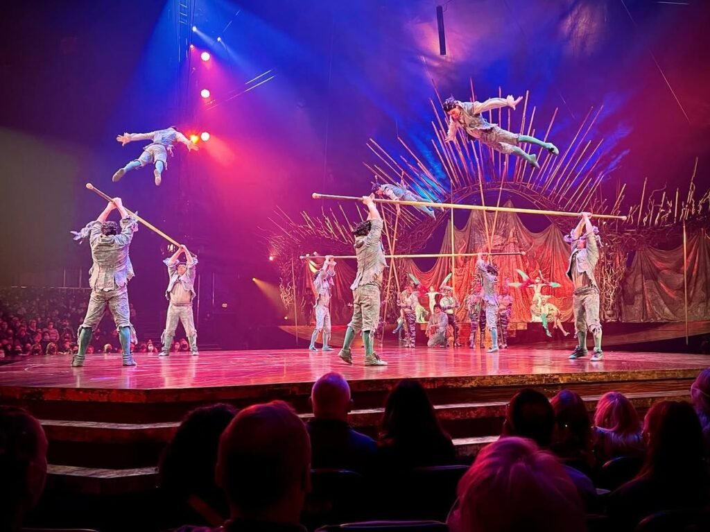 Circus performers executing aerial stunts with colorful lighting and an audience watching from below.