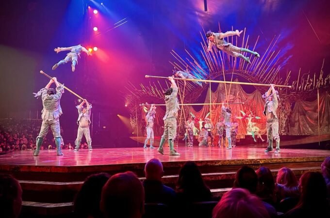 Circus performers executing aerial stunts with colorful lighting and an audience watching from below.