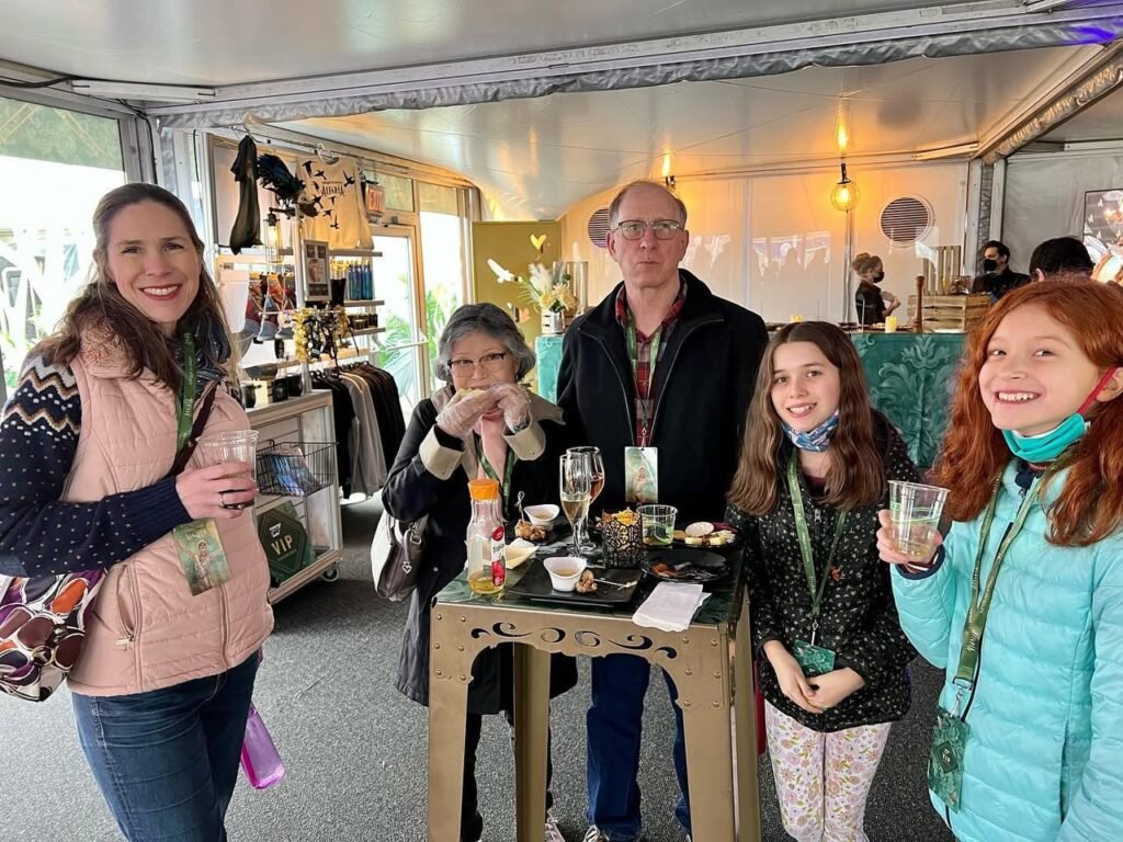 A group of people smiling and holding drinks at a pop-up shop with a table and display cabinets in the background.