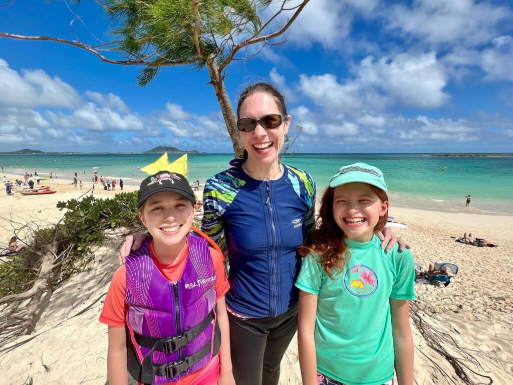 A family of three enjoying a sunny day at Turbo Beach in the Whitsundays, with turquoise water and white clouds behind them.