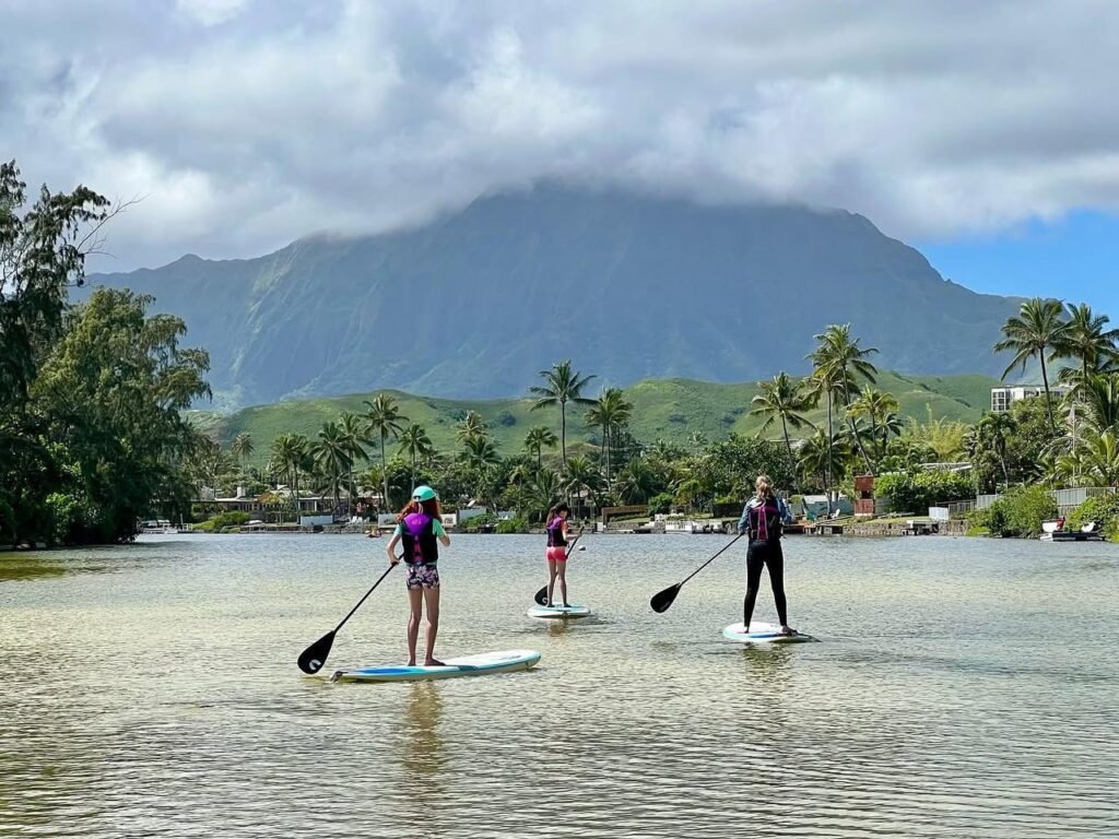 Several people paddleboarding on calm water with a stunning mountain backdrop and tropical vegetation.