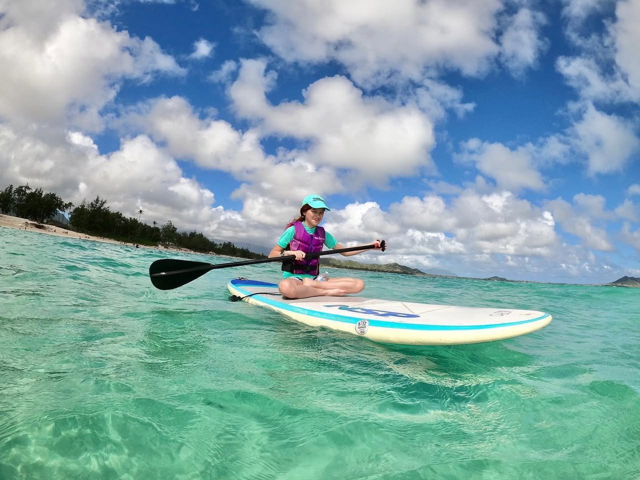 A wide-angle shot of a person on a paddleboard in clear turquoise water under a blue sky, with a second person paddling nearby.