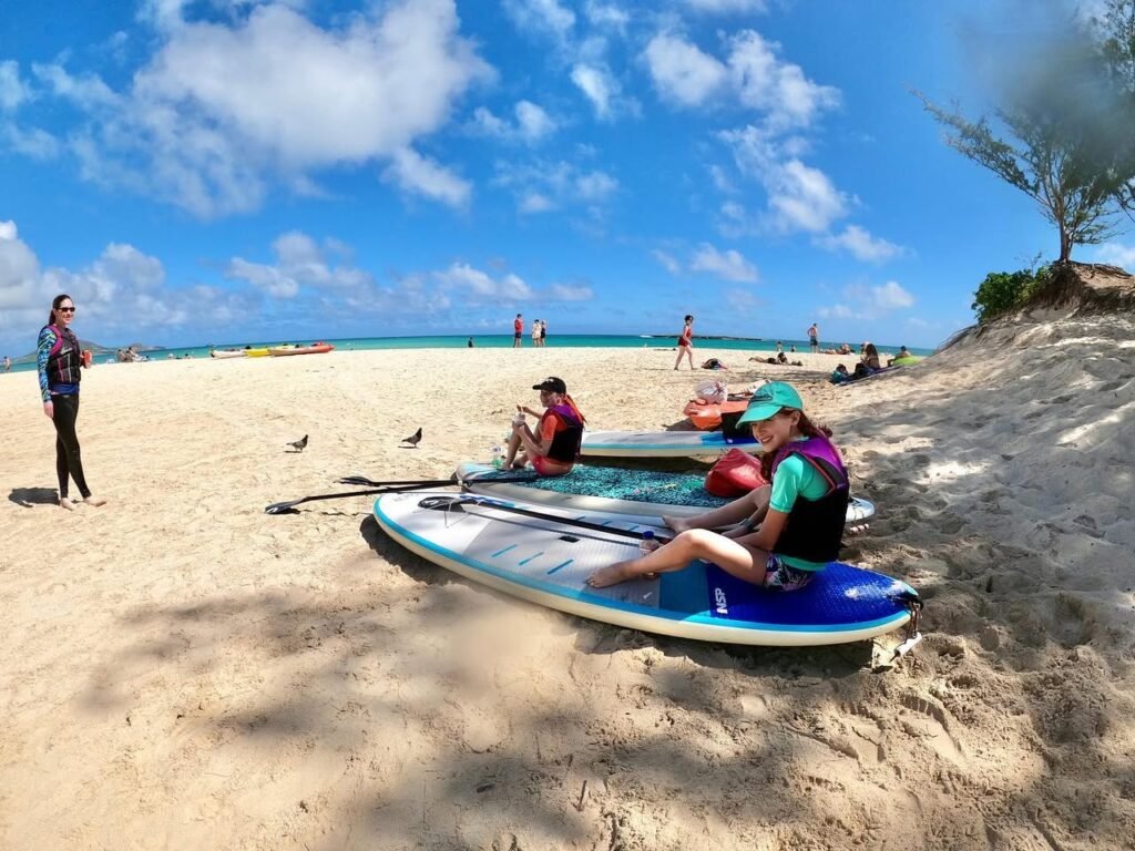People prepare to kayak on a sunny beach with clear blue skies and ocean views.