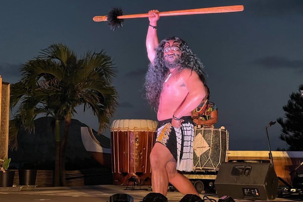Entertainer performing on stage with a long rooster-tail trous, vintage microphone, and large shell.