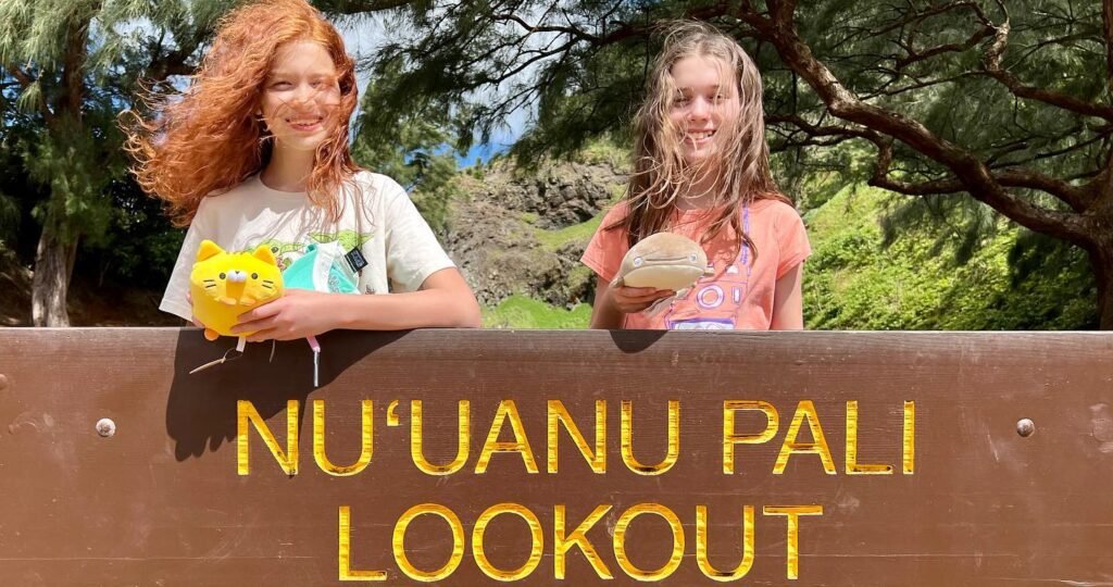 A group photo taken behind a sign at the Nuuanu Pali Lookout with a sunny outdoor background.