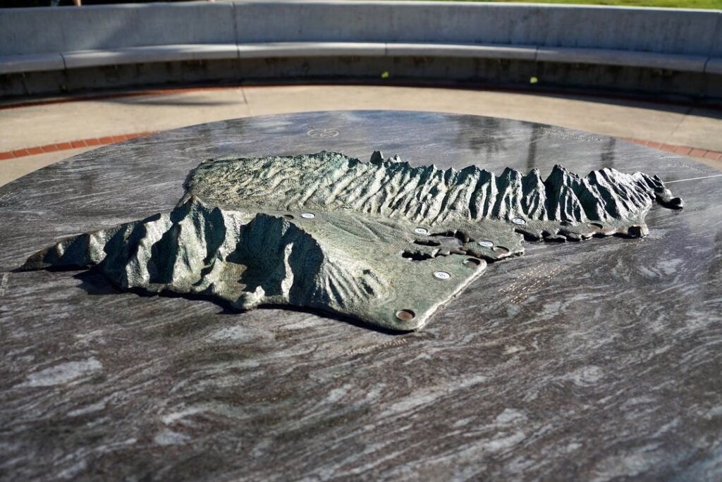A silver zebra-shaped metal sculpture resting on a large circular granite pedestal outdoors.