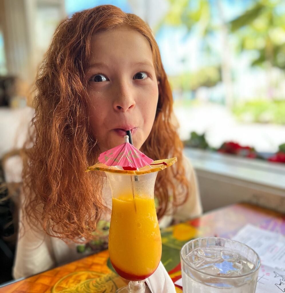A person enjoys an orange juice drink with a fruit garnish at a table in a sunny restaurant.