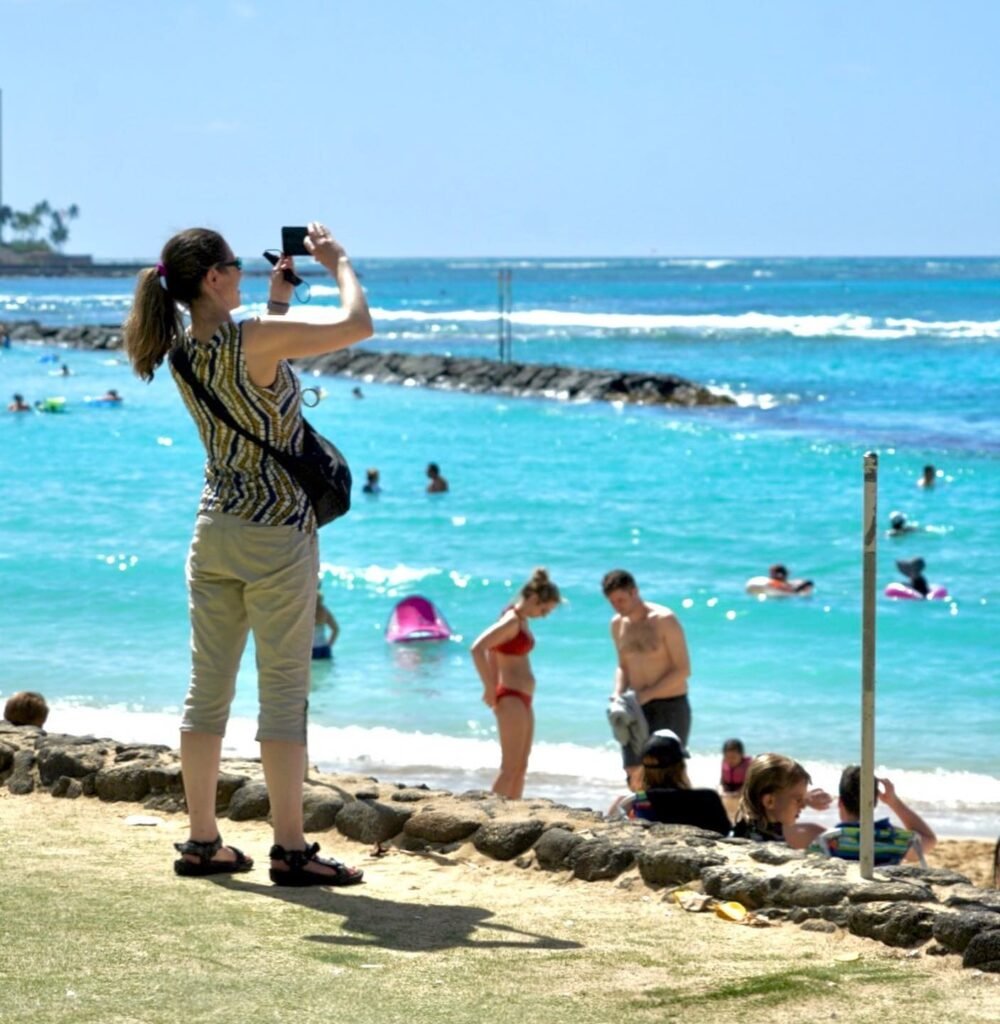 A close-up photo of a person using a smartphone to take pictures at a beach.