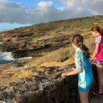 Waikiki View of dramatic rocky sea cliffs along a coastline. People standing near the edge taking photos of the ocean.