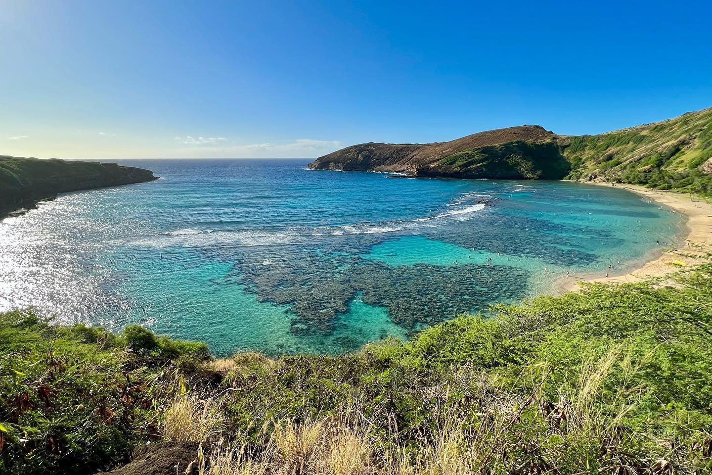 Hanauma Bay A scenic coastal landscape featuring clear turquoise waters, secluded sandy beaches, and hilly green coastlines under a bright blue sky.