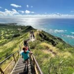 Kualoa Ranch Hikers ascending grassy cliffs to a coastal viewpoint in Hawaii with turquoise ocean views.
