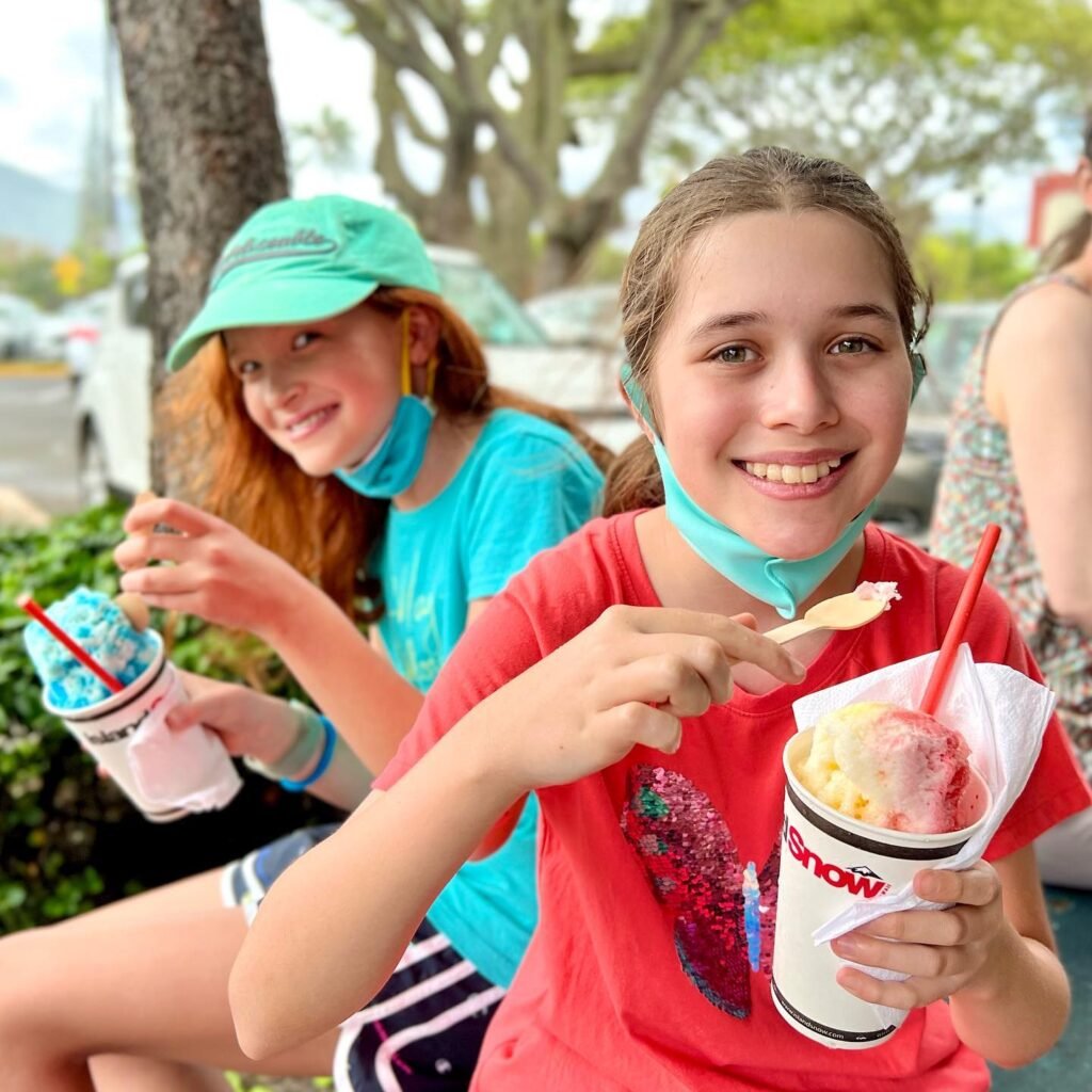 Two young people enjoying colorful snow cones outdoors.