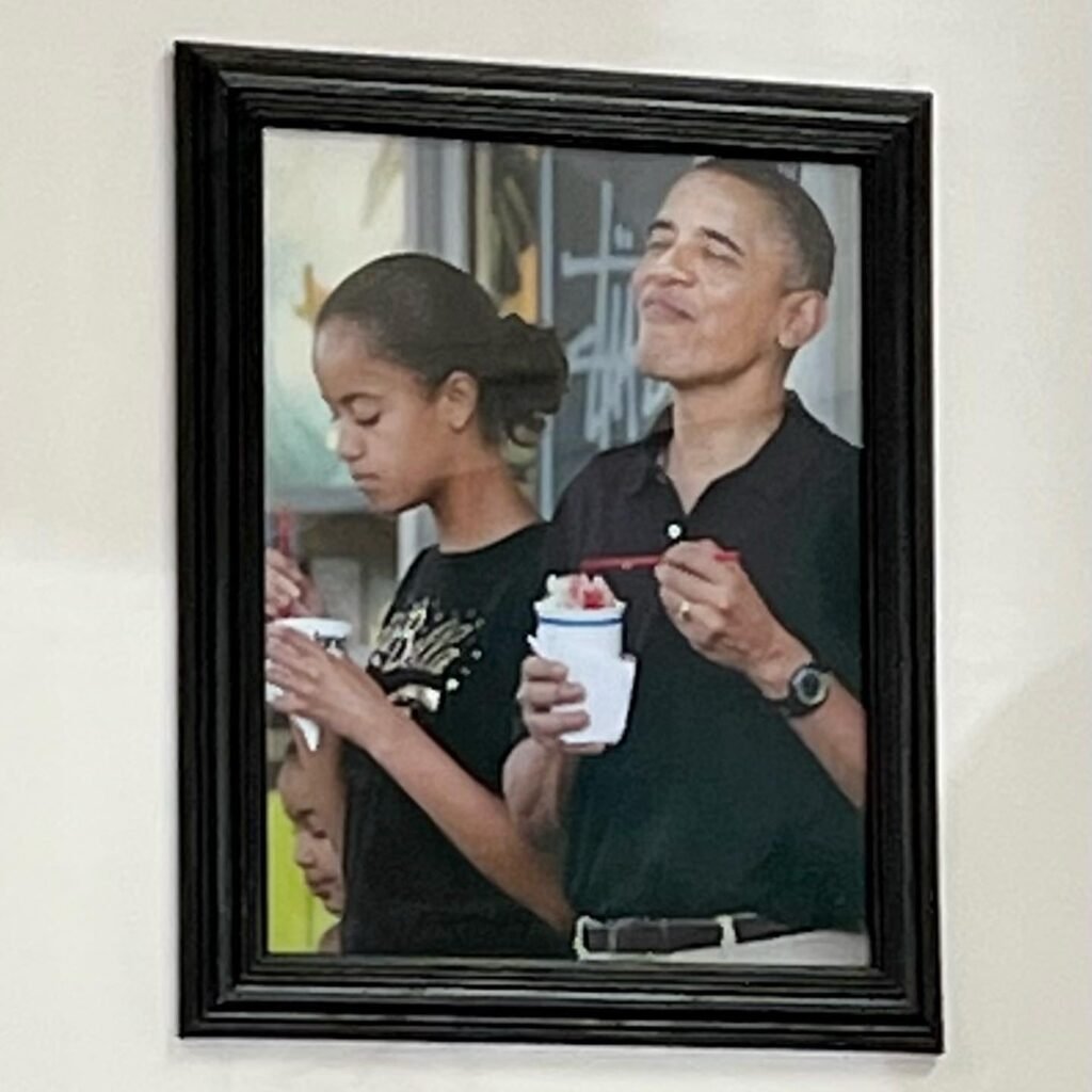 Framed photo on a white wall showing a family enjoying a meal together. Another framed photo is visible below it.
